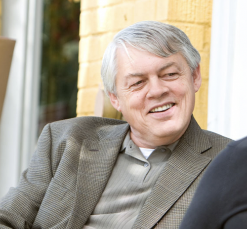 White man, gray hair, green-gray collared shirt with a striped blazer.